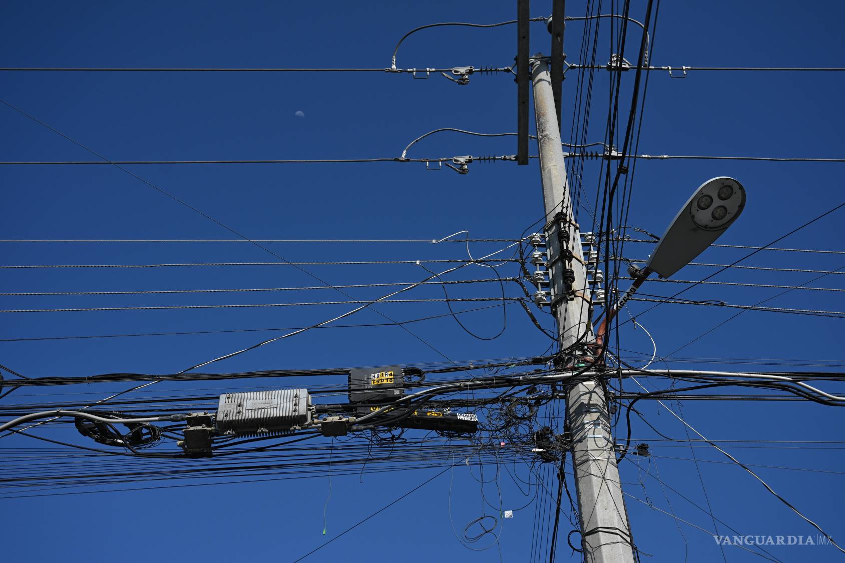 $!Sobre el azul intenso del cielo, postes, líneas eléctricas y cables de telecomunicaciones forman una geometría irregular. La infraestructura de distintas redes comparte espacio, se superpone y termina por confundirse en una sola estructura.