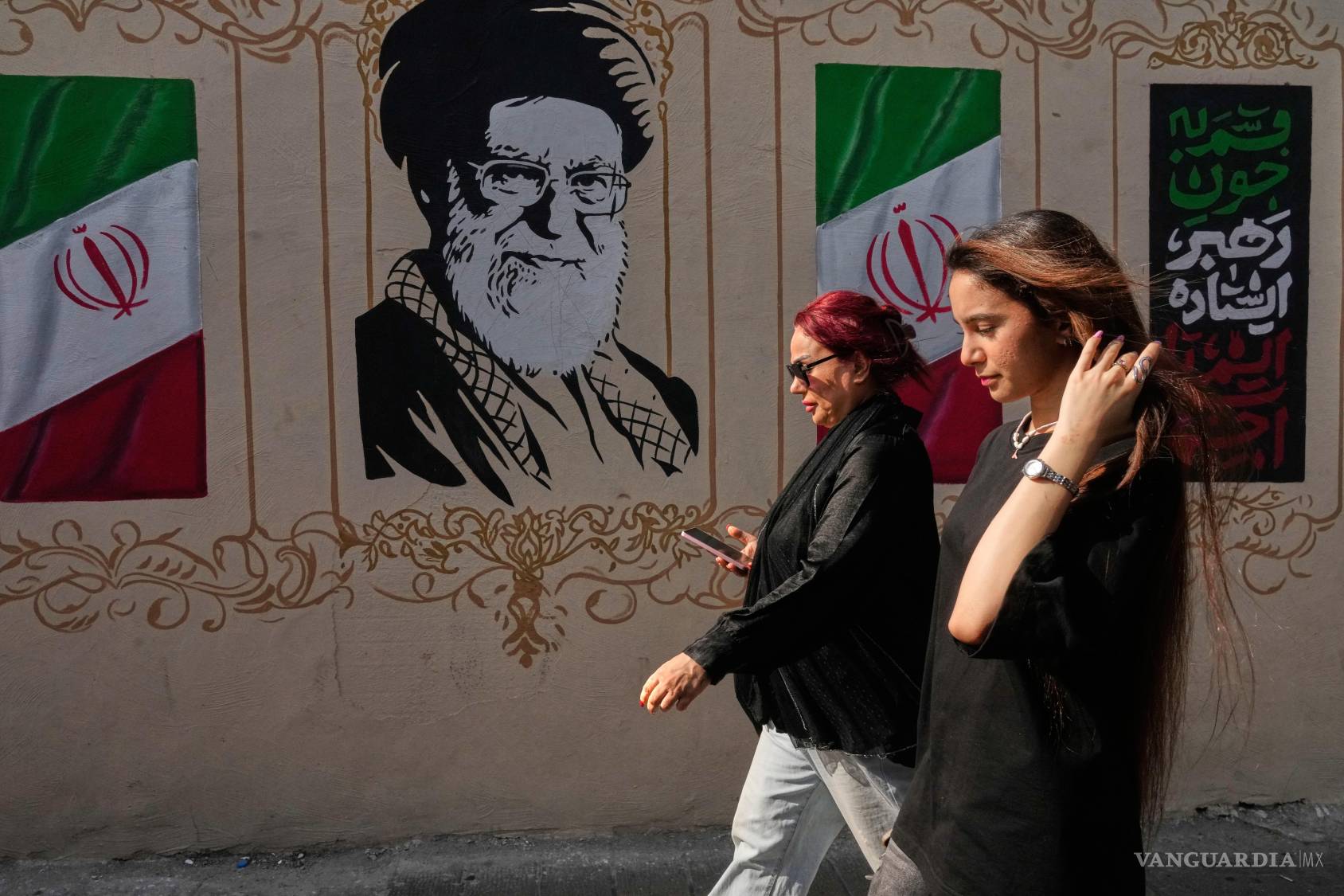 $!Dos mujeres caminan frente a una imagen del difunto líder supremo de Irán, ayatolá Ali Jamenei en el centro de Teherán, Irán.