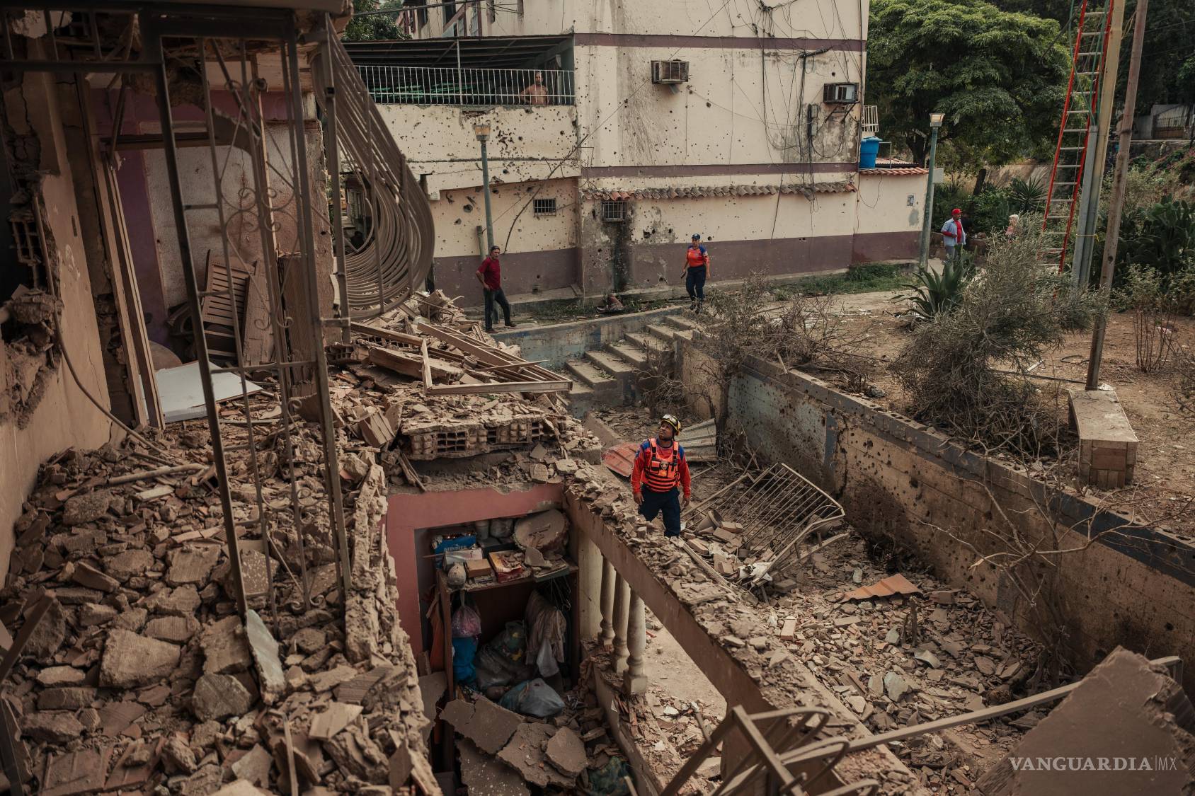 $!Trabajadores de defensa civil y residentes locales inspeccionan los daños en un edificio de apartamentos dañado por un ataque aéreo estadounidense en Catia La Mar, a las afueras de Caracas.