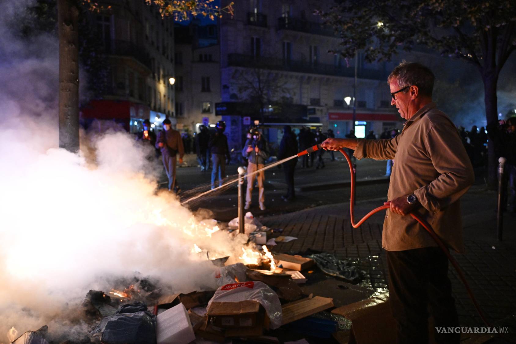 $!Un hombre intenta sofocar un incendio durante enfrentamientos entre manifestantes y la policía en París, el domingo 18 de octubre de 2026.