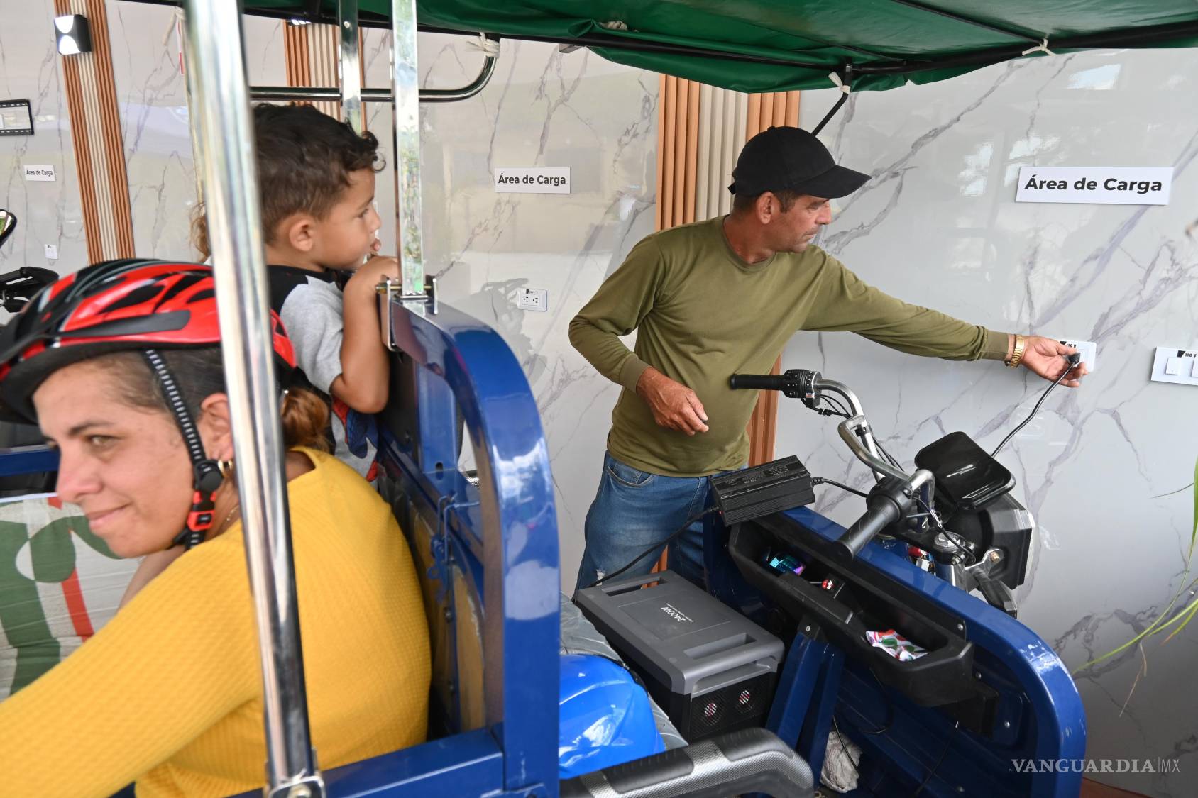 $!Lorenzo Ravelo, a la derecha, enchufa su triciclo eléctrico en una estación solar en Santa Clara, Cuba.