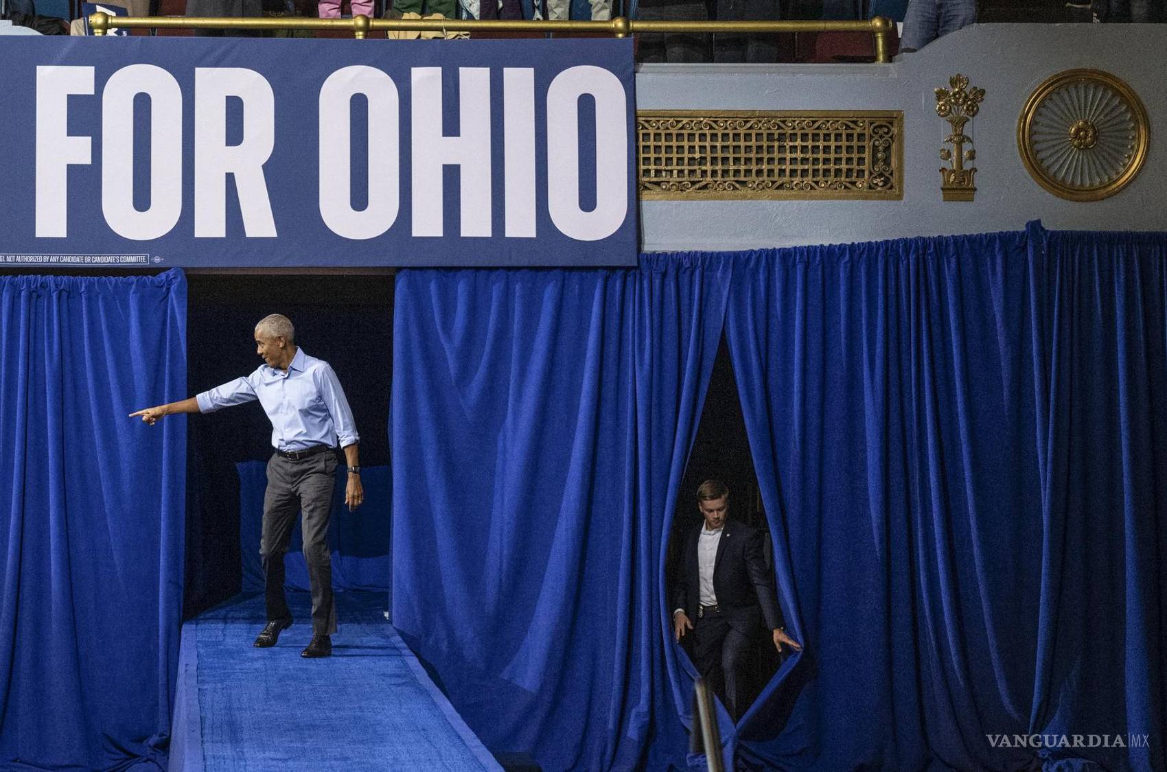 $!El expresidente Barack Obama, llega a un mitin de campaña, mientras un miembro de su equipo de seguridad aprovecha una abertura entre las cortinas, en Cleveland, Ohio.