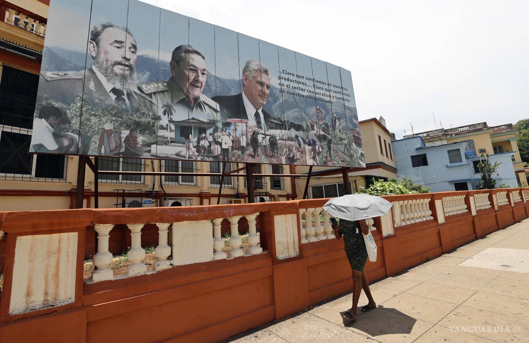 $!Una mujer camina a las imágenes del presidente de Cuba, Miguel Diaz-Canel , el general y expresidente Raúl Castro y el fallecido expresidente Fidel Castro.