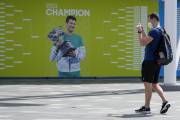 Aficionado saca una foto frente a un cartel con la imagen del campeón defensor Novak Djokovic previo al Abierto de Australia en Melbourne Park. FOTO: Mark Baker/AP