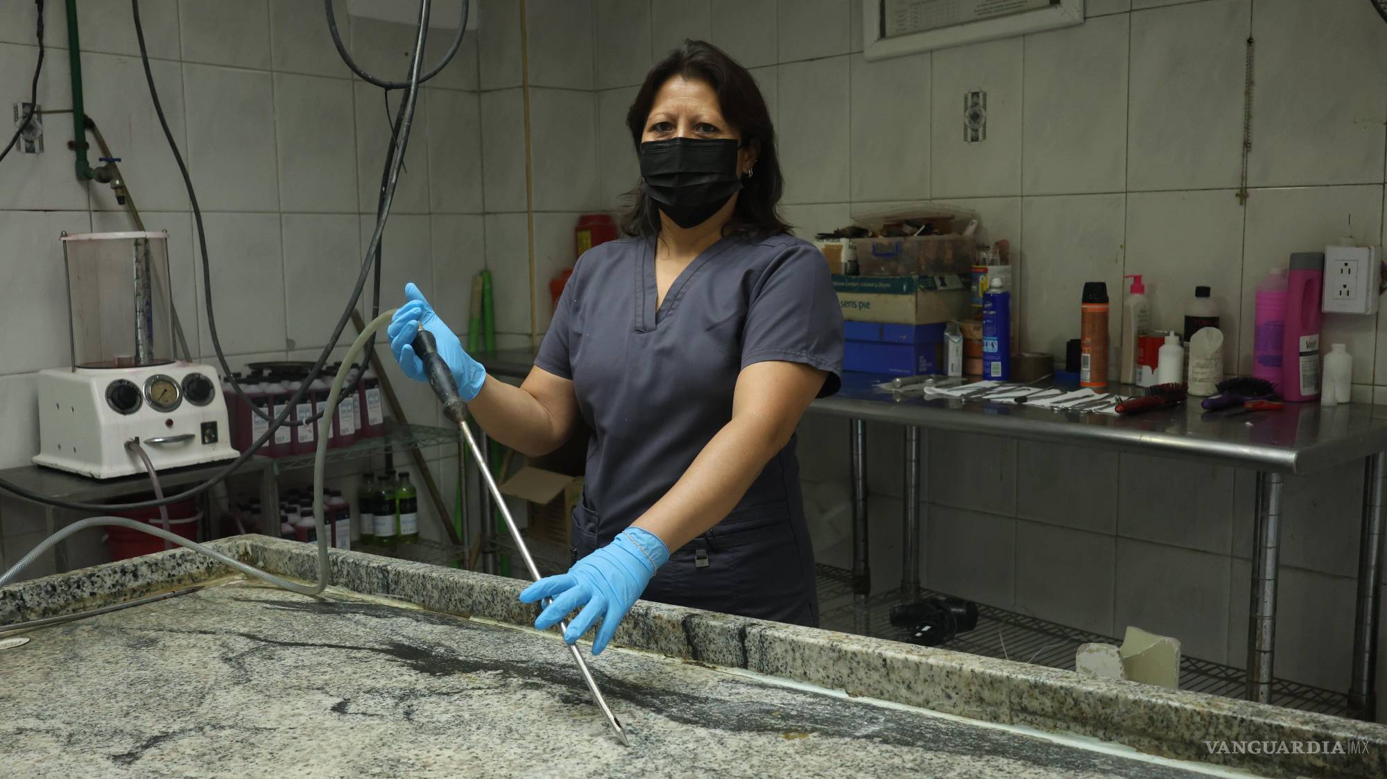 $!Mary sostiene un instrumento que perfora el cuerpo y, a través de pequeños orificios en la punta, inyecta los químicos a presión para conservarlo.