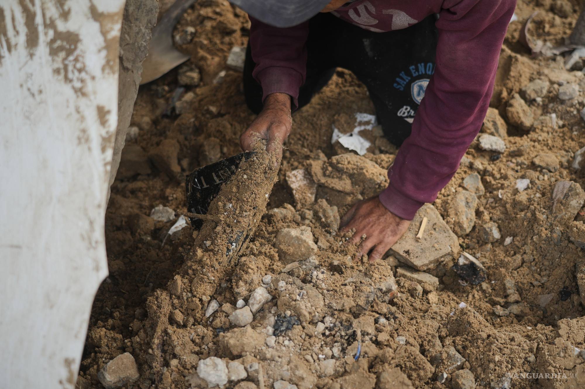 $!Un familiar de Mahmoud Hammad le ayuda a buscar los restos de su esposa, Nema Hammad, que sigue atrapada bajo los escombros de su casa.