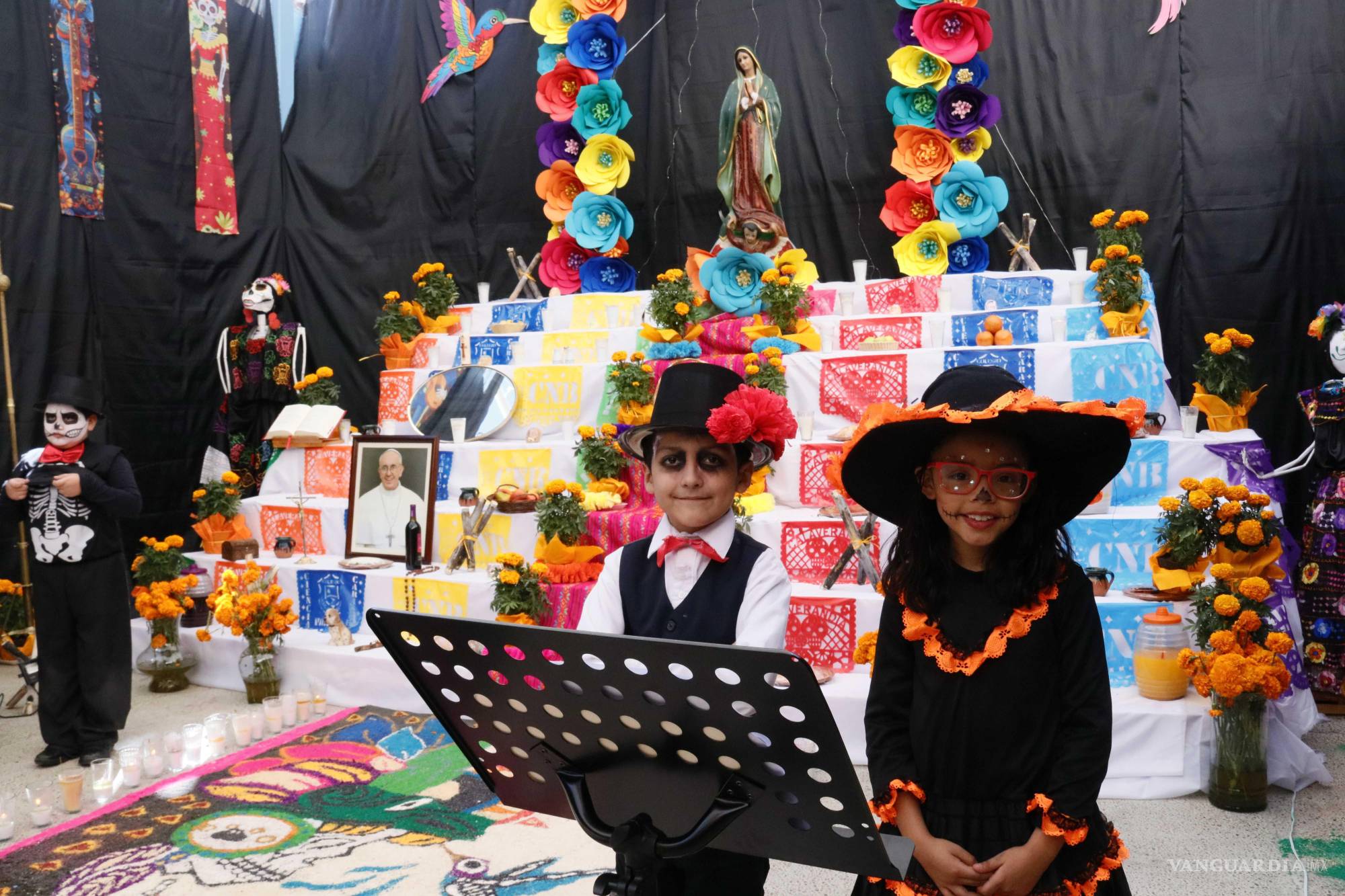 $!Altar inspirado en la leyenda del colibrí y el Mictlán, con tapete de aserrín, arco floral y escenografía del bosque de luciérnagas de Val’Quirico, Tlaxcala.