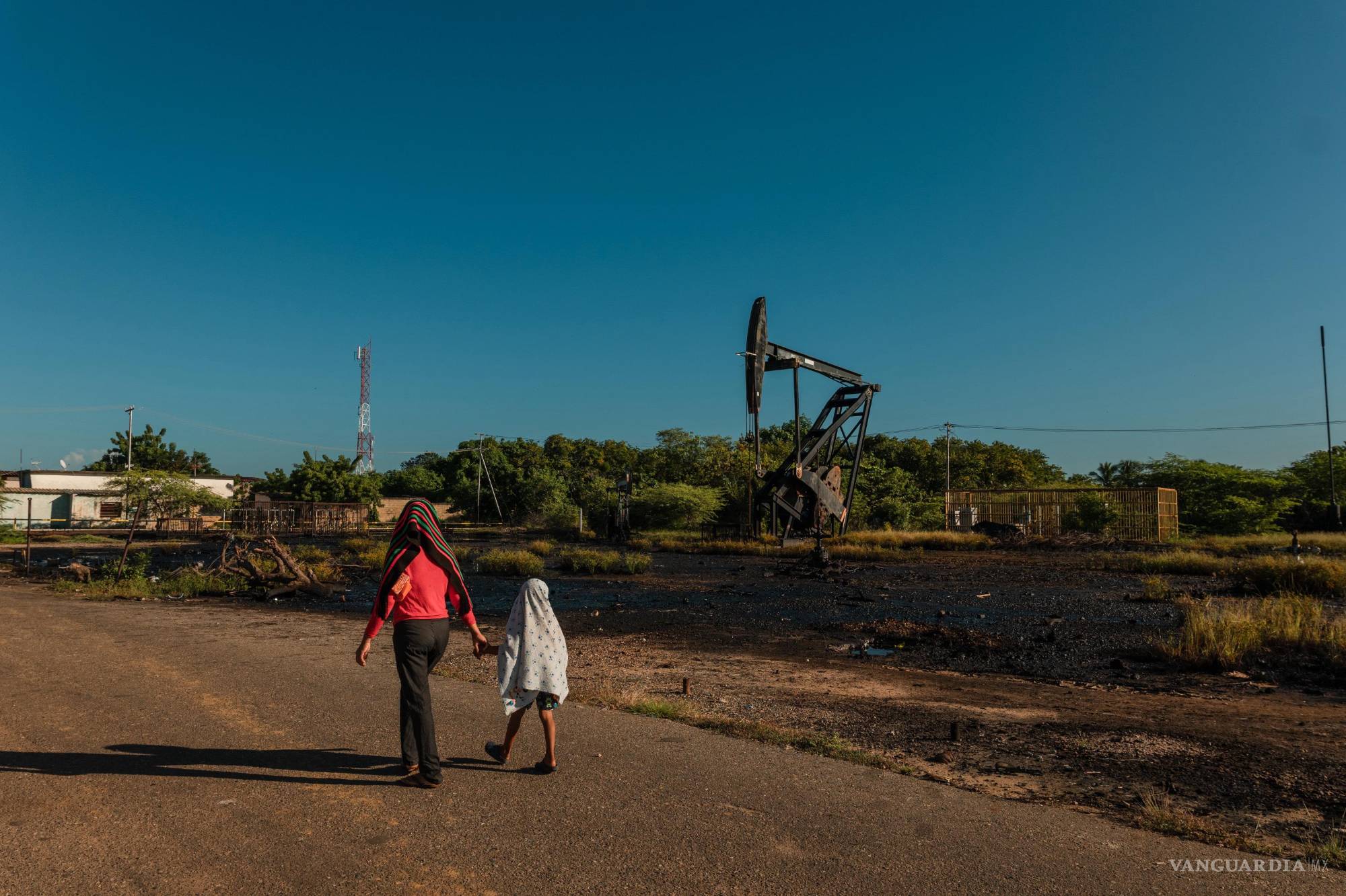 $!Civiles caminan cerca de una infraestructura petrolera dañada en Venezuela; las incursiones aéreas estadounidenses han impactado zonas estratégicas del país.