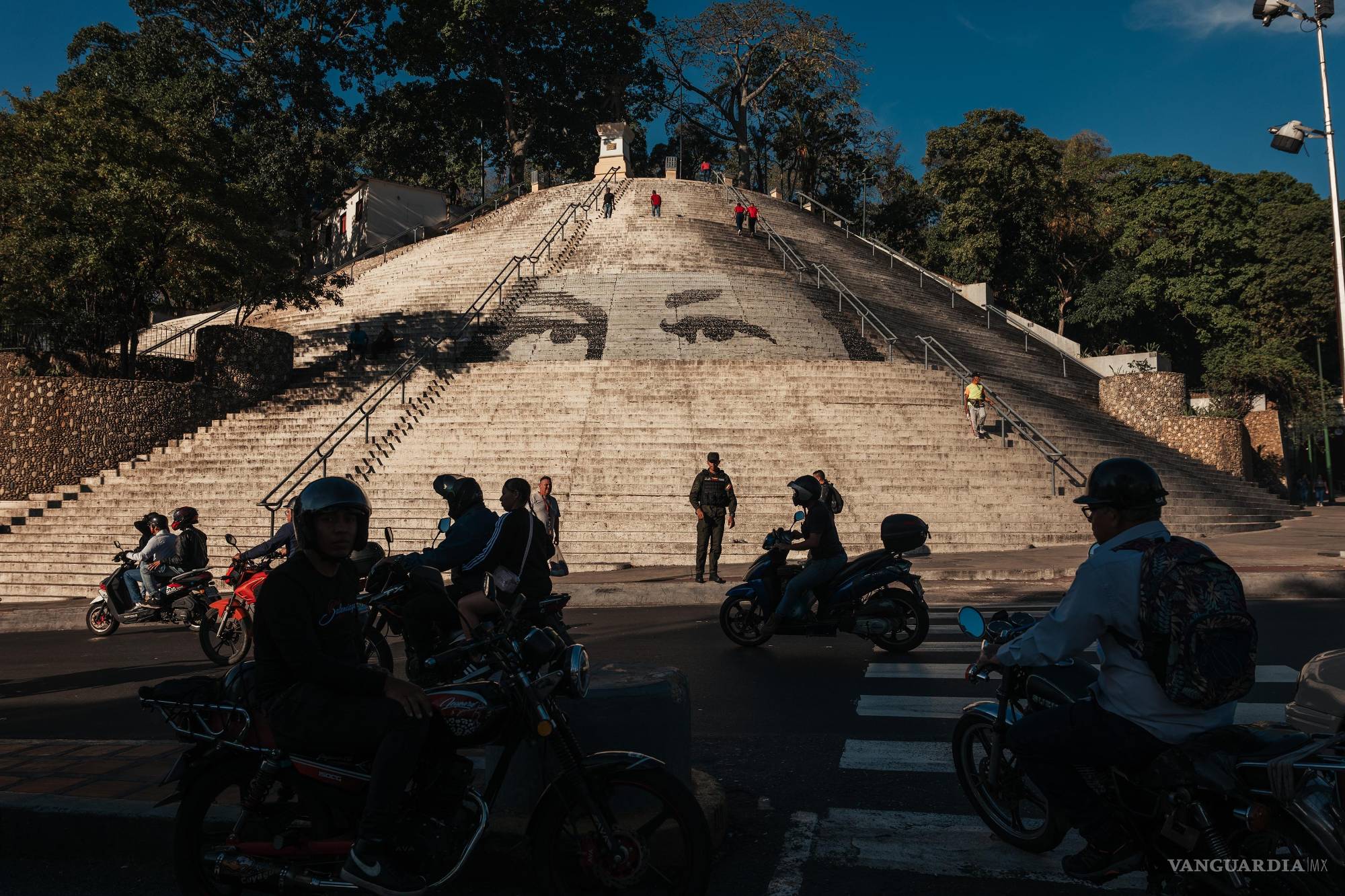 $!Motociclistas transitan frente a las emblemáticas escaleras con la mirada de Hugo Chávez en Caracas.