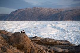 Estudiantes investigadores de la NYU se sientan sobre una roca con vistas al glaciar Helheim, en Groenlandia, el 16 de agosto de 2019.