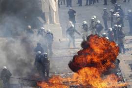 Agentes de la policía antimotines intenta evitar las llamas de una bomba molotov arrojada afuera del Parlamento durante una protesta en el centro de Atenas, en el segundo aniversario del peor desastre ferroviario de Grecia, el viernes 28 de febrero de 2025. FOTO: