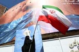 Una mujer con velo sostiene la bandera nacional de Irán frente a una enorme valla publicitaria antiestadounidense en la plaza Valiasr de Teherán.