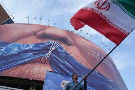 Un hombre ondea una bandera iraní para una campaña progubernamental bajo un cartel que muestra el estrecho de Ormuz y los labios del presidente de Estados Unidos, Donald Trump en una Teherán, Irán.