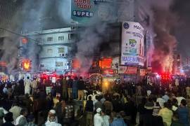 Gente reunida mientras los bomberos intentan conrolar un enorme incendio en un centro comercial de varias plantas en Karachi, Pakistán. FOTO: