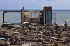 Personas caminan frente a una casa destruida, este jueves en el poblado de Guamá, Santiago de Cuba.
