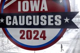 Un hombre cruza la calle debajo de un cartel de los Caucus de Iowa en el centro de Des Moines, Iowa.
