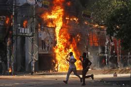 Los hombres corren frente a un centro comercial que fue incendiado durante una manifestación contra la Primera Ministra Sheikh Hasina.