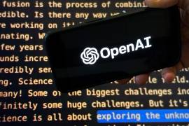 El logotipo de OpenAI aparece en un teléfono móvil frente a una pantalla que muestra parte del sitio web de la empresa.