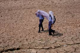 Niños en edad escolar se cubren la cabeza con toallas de algodón para protegerse del calor abrasador de la tarde mientras caminan por un campo reseco en las afueras de Jammu, India,