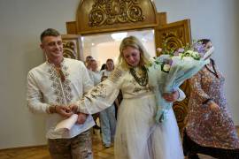 La recién casada Liudmyla Ryzhak (a la derecha) y su esposo, Leonid Ryzhak, salen tras contraer matrimonio, después de un ataque ruso con misiles y drones en Kiev, Ucrania.