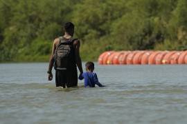 Migrantes pasan junto a grandes boyas que se utilizan como barrera fronteriza flotante en el Río Grande, el 1 de agosto de 2023, en Eagle Pass, Texas.