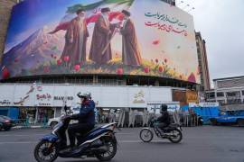 Motos pasan por delante de un cartel con la imagen del difunto líder supremo de Irán, el ayatolá Ali Jamenei (c), entregando la bandera del país a su hijo y sucesor, el ayatolá Moytabá Jamenei (d), en Teherán, Irán.