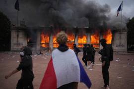 Un manifestante se envuelve con una bandera francesa frente a la oficina de turismo en llamas durante una protesta contra el aumento del costo de vida y en solidaridad con las quejas de los estudiantes en Lyon, Francia, el sábado 17 de octubre de 2026.
