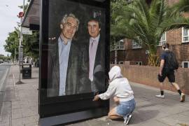 Una activista coloca un cartel del ahora presidente Donald Trump con Jeffrey Epstein, en una parada de autobús cerca de la embajada de Estados Unidos en Londres.
