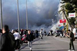 El humo se eleva mientras los transeúntes observan tras un ataque israelí que impactó un edificio cerca de la carretera del aeropuerto en Beirut.