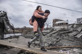 Un hombre carga a una mujer mientras cruzan un camino improvisado mientras huyen de la ciudad de Irpin, Ucrania. AP/Oleksandr Ratushniak