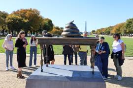 Personas observan una figura en bronce de un escritorio con un excremento encima, instalado en el National Mall cerca del Capitolio en Washington.