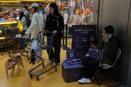 Clientes llevan a sus perros a una tienda de mascotas mientras un dependiente promociona el vehículo eléctrico Audi E5 Sportback en un rincón del establecimiento en Pekín.