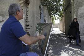 El pintor Hassan Naderali saluda a una residente mientras pinta un edificio antiguo en el barrio histórico de Oudlajan, en Teherán, Irán.