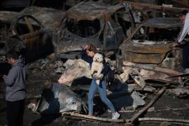 Una mujer sostiene a su perro mientras camina junto a coches calcinados un día después de un ataque aéreo israelí en Beirut, Líbano, el jueves 9 de abril de 2026.
