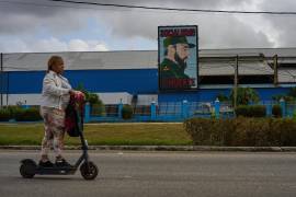 Una mujer pasa en patineta eléctrica frente a una fábrica que exhibe una imagen del fallecido líder cubano Fidel Castro, con la leyenda “Socialismo o muerte”, en La Habana, Cuba.