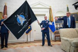 El general John “Jay” Raymond, comandante del Comando Espacial (i), yel suboficial mayor Roger Towberman (c) sostienen la bandera de la Fuerza Espacial junto con Donald Trump en la Casa Blanca.
