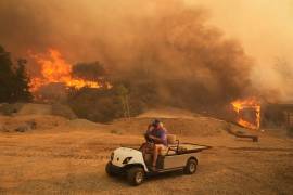 Un residente sale de su propiedad en un carrito de golf mientras el incendio Canyon arde el 7 de agosto de 2025 en Hasley Canyon, California.
