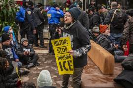 Una activista sostiene un cartel en el vestíbulo de un hotel con el mensaje: “Hilton: dejen de alojar al ICE”, reflejando la toma de espacios privados para la protesta.