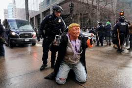 A person wearing a Trump mask is told to get up by a Minneapolis Police officer Saturday, Jan. 17, 2026, in Minneapolis. (AP Photo/Yuki Iwamura)