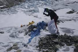 Un miembro del equipo financiado por el gobierno de Nepal valiéndose de un pico para retirar basura congelada en camino al monte Everest.