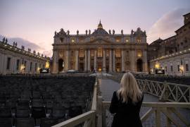 Una mujer mira hacia la Plaza de San Pedro en la Ciudad del Vaticano, donde las pantallas anuncian el rezo del rosario por la salud del Papa Francisco.