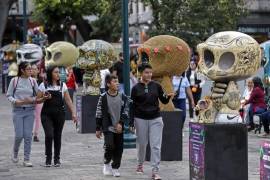 Personas observan piezas de la exposición “Me lleva la huesuda” en el zócalo de la ciudad de Puebla (México).
