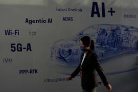 Una mujer pasa junto a un panel informativo que muestra un vehículo eléctrico impulsado por inteligencia artificial (IA) en el Auto China 2026, en Pekín,