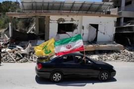 Residentes desplazados portan banderas de Irán y Hezbolá al pasar junto a un edificio destruido que fue alcanzado por un ataque aéreo israelí en la aldea sureña de Chehabiyeh, Líbano.