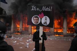 Un manifestante sostiene una pancarta con una foto del presidente francés Emmanuel Macron y una guillotina frente a una oficina de turismo en llamas durante una protesta contra el aumento del costo de vida.