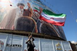 Un hombre iraní ondea la bandera nacional de Irán frente a una gran valla publicitaria que muestra un retrato del difunto líder supremo iraní, el ayatolá Ali Khamenei, en la plaza Valiasr de Teherán, Irán.