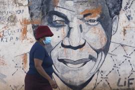 Una mujer con mascarilla pasa junto a un mural del expresidente de Sudáfrica, Nelson Mandela, en Katlehong, al este de Johannesburgo, Sudáfrica.