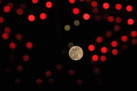 Última luna llena del año, conocida como luna Fría, emerge en el horizonte detrás de unas luces navideñas.