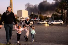 Una familia llega para celebrar la caída del gobierno sirio con humo de fondo en Damasco, Siria, el 8 de diciembre de 2024.