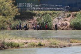 Un grupo de migrantes trata de cruzar la alambrada instalada a orilla del rio Bravo, en la frontera de Eagle Pass, Texas.